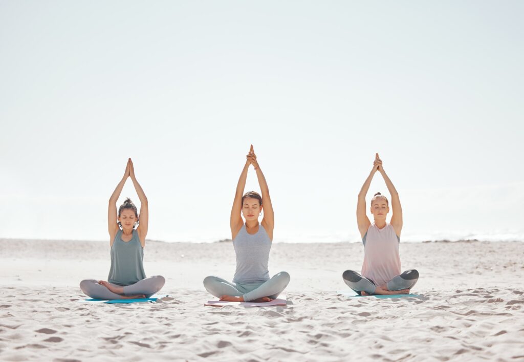 Zen, meditation and yoga at the beach with women for wellness, fitness and health. Stretching, lotu